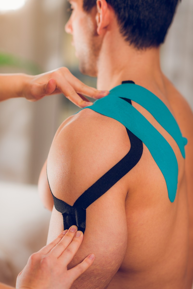 Shoulder treatment with kinesio tape man having his shoulder bandaged by a Centre Philae physiotherapist
